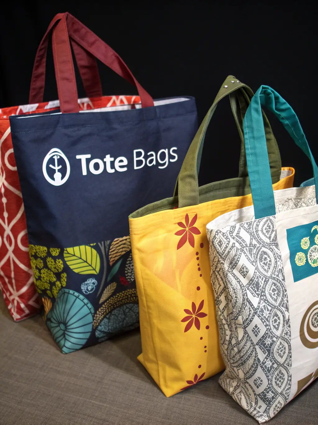 A visually appealing image featuring a collection of custom-designed tote bags with different prints, patterns, and logos, arranged in an eco-friendly setting, showcasing the versatility and sustainability of PERSONTEES' tote bag design services.